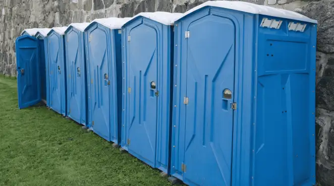 Row of blue portable toilets lined up on grass against a stone wall for event sanitation in Columbus, OH