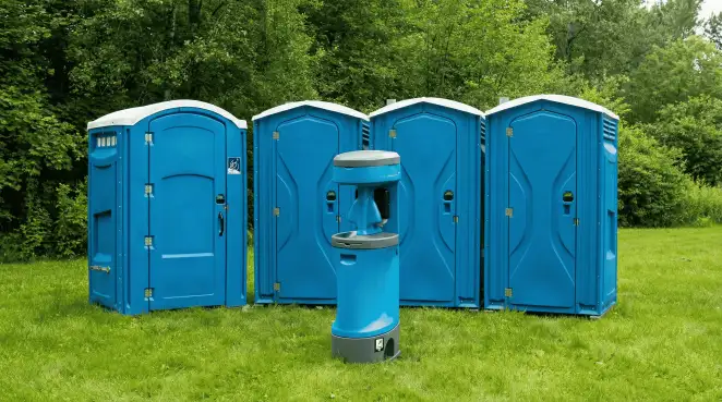 Four blue portable toilets and a matching hand washing station on grass near trees, a common sight at local outdoor events in Columbus, OH