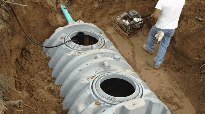 Septic tank installation showing a technician compacting soil around a new poly septic tank in an excavation pit in Columbus, OH